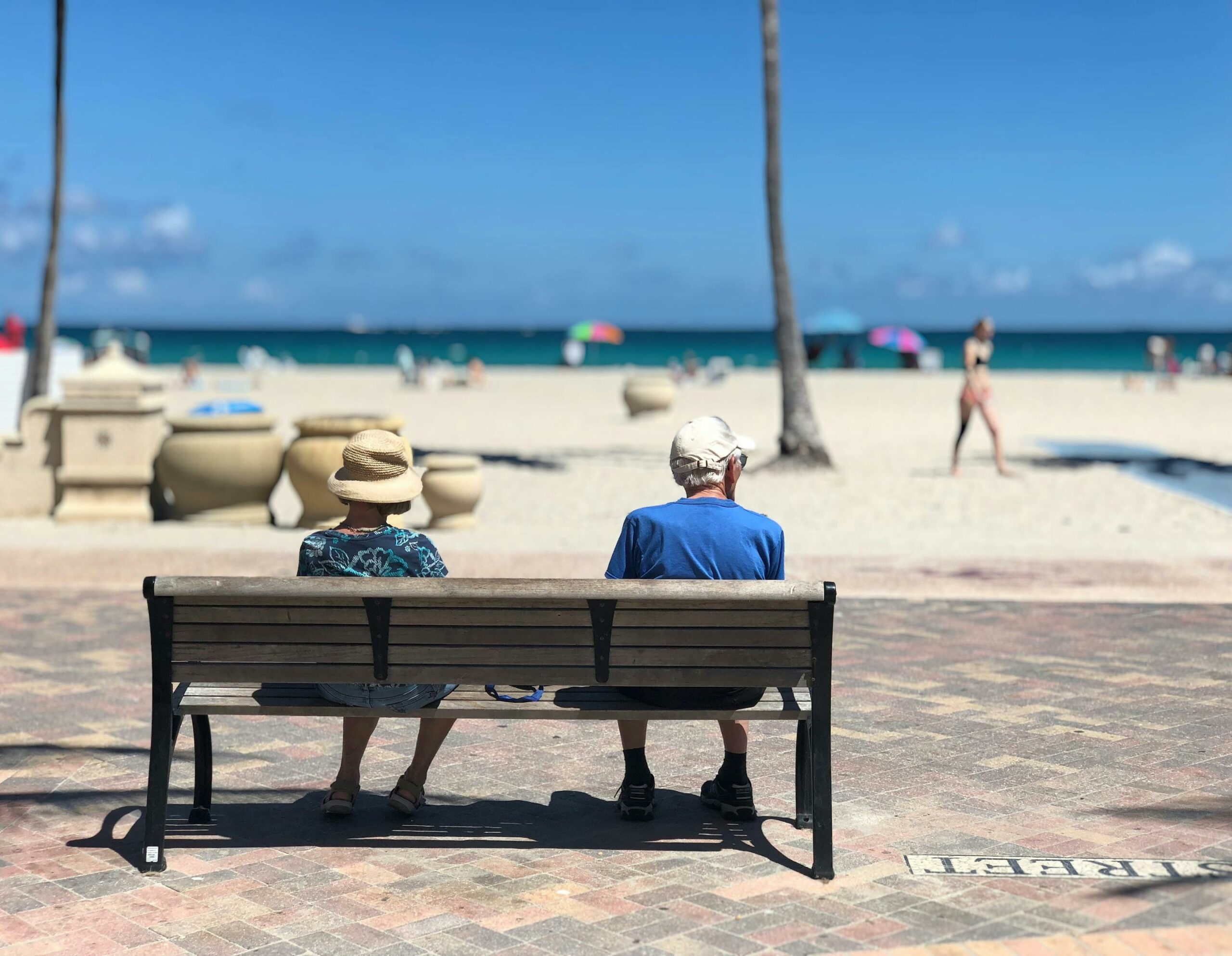 Due persone anziane in estate sedute su una panchina di spalle che guardano il mare